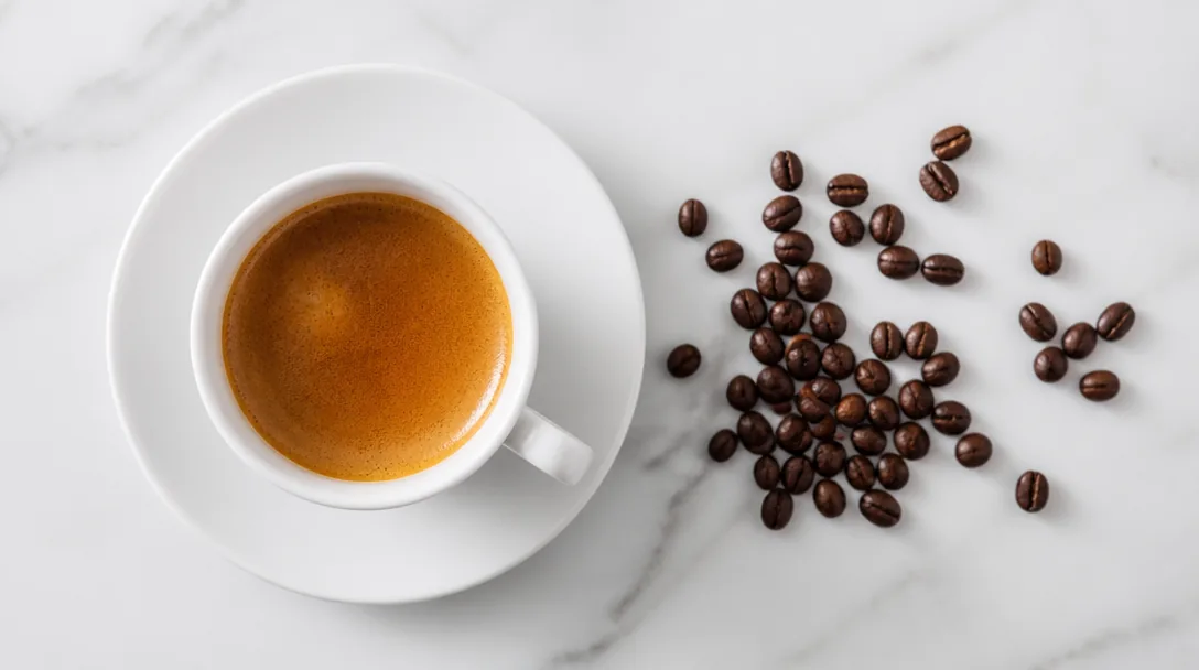 Nybryggd espresso i vit keramikkopp med kaffebönor bredvid på vit yta, uppifrån-perspektiv