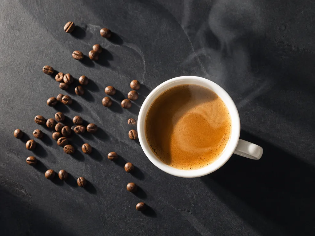 Ovanifrån: ångande espressokopp och kaffebönor på en mörk skifferskiva i naturligt morgonljus